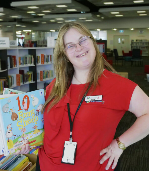 Kailtin in the Library smiling holding a book. 