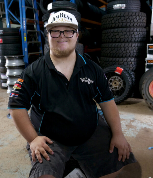 Tane smiling at his workplace, wearing the uniform.