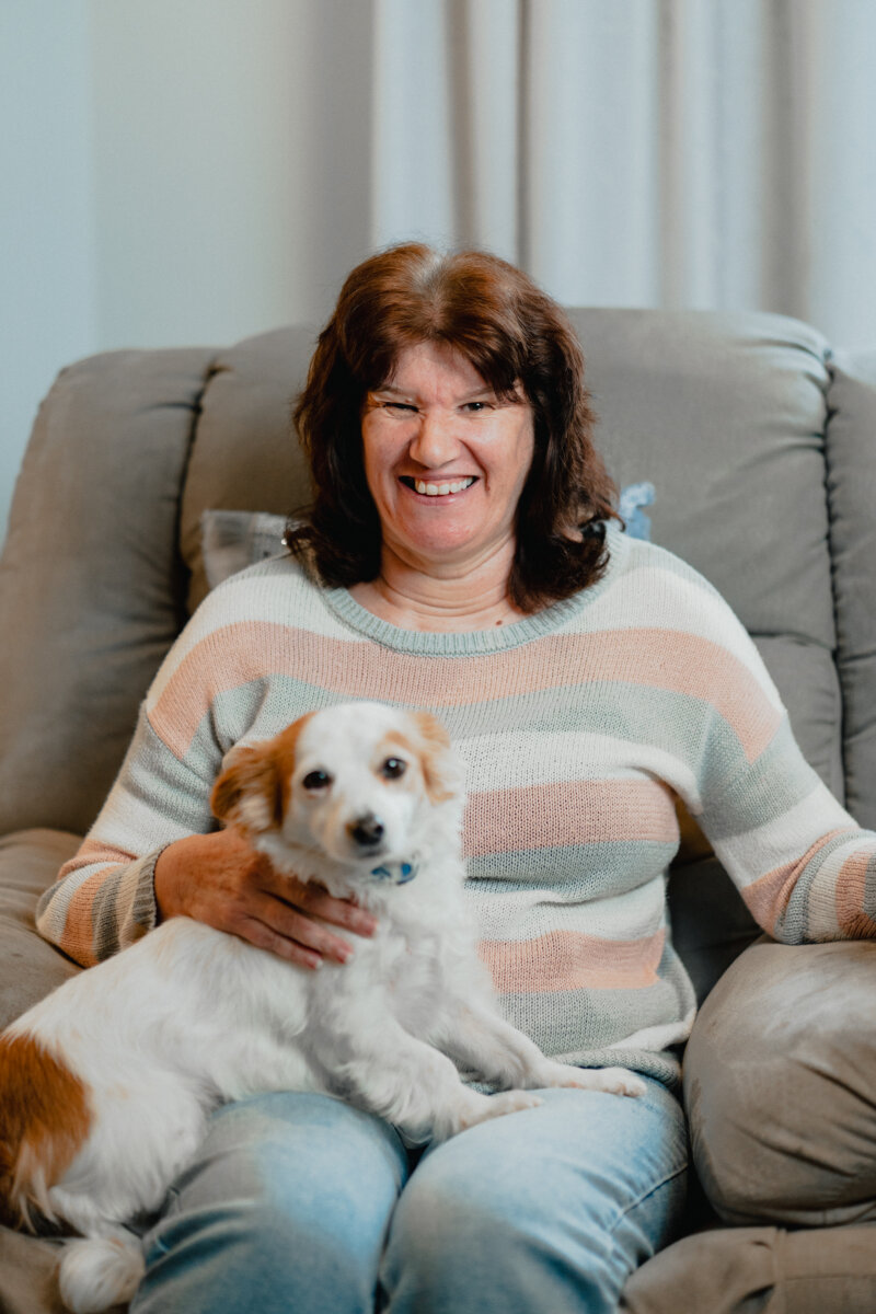 Kathy smiling on her couch with dog on her lap.